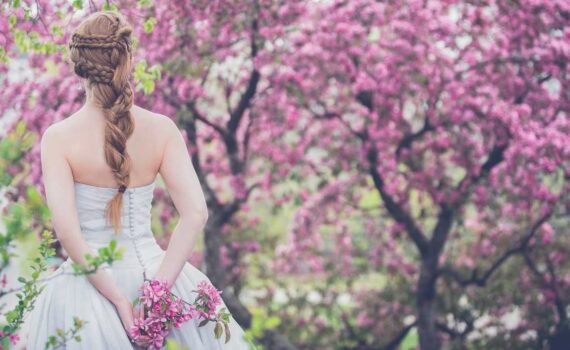 [Uber En="spring*wedding*bride*standing*in*front*of*blooming*trees*with*a*romantic*hairstyle" De="Frühlingshochzeit*Braut*vor*blühenden*Bäumen*mit*romantischer*Flechtfrisur"]