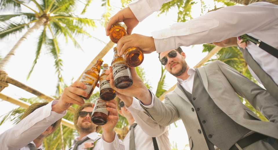 "Sommerhochzeit mit Freunden des Bräutigams, die unter Palmen mit Bierflaschen anstoßen"