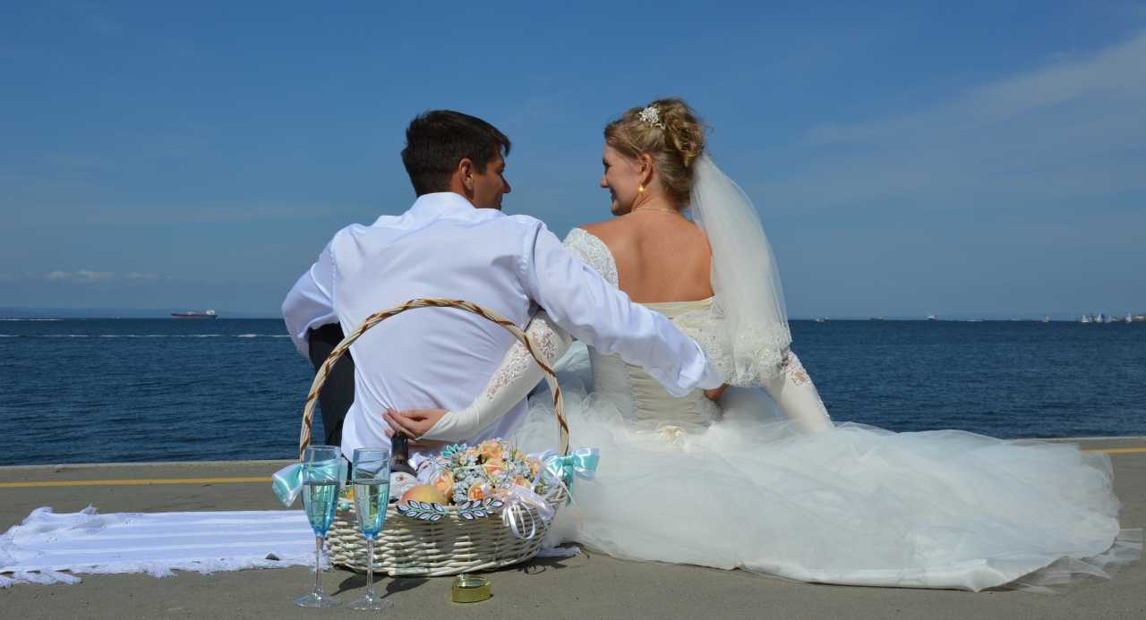 [Uber En="summer*wedding*couple*sitting*on*a*beach*looking*out*to*sea*with*a*picnic*basket*of*flowers*fruit*and*champagne" De="Sommerhochzeit*Paar*am*Strand*mit*Blick*aufs*Meer*neben*einem*Picknickkorb*mit*Blumen,*Obst*und*Sekt"]